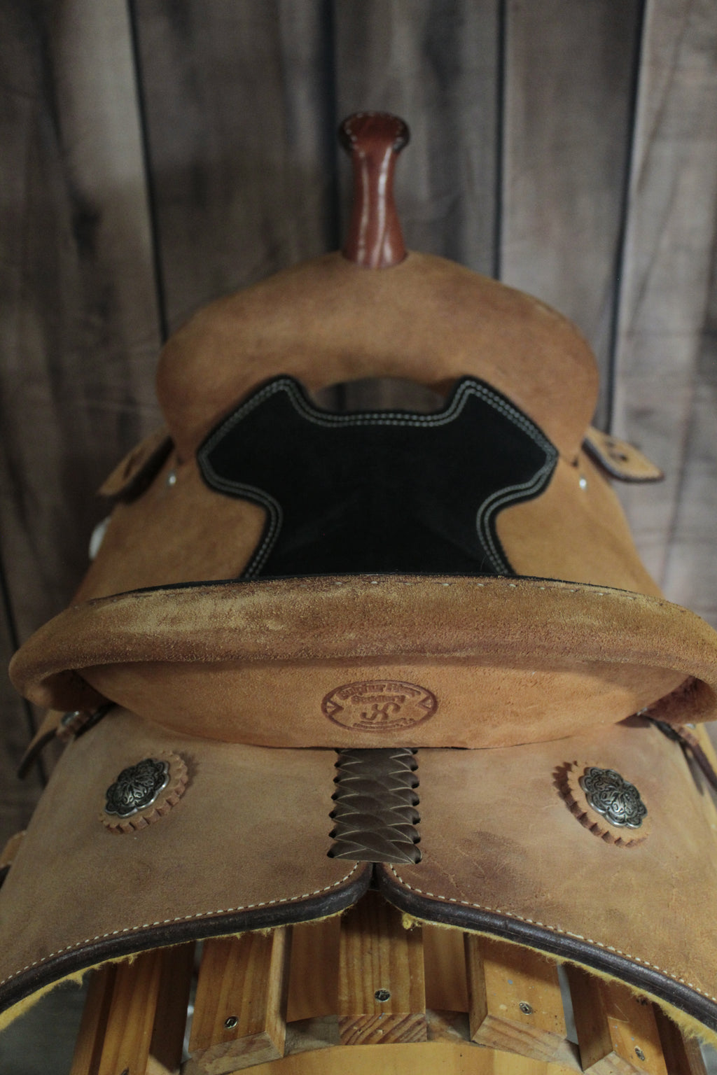 Close-up of a brown leather saddle with decorative conchos on a wooden background